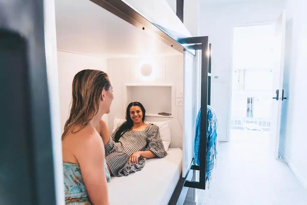 two women in a bunk bed at a hostel talking and smiling